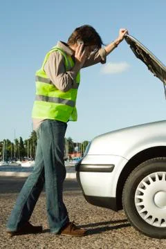 Man making phone call with cell phone while evaluating car broken down on side Stock Photos