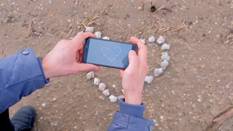 Man making photo of heart from shell on sandy beach using phone, hands closeup. Stock Footage 117906873