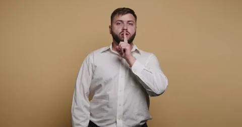 Man making a shushing gesture against a simple background while wearing a w.. Video stock 326797450