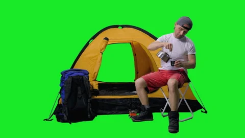 Man making tea while sitting near tourist tent with backpack in summer camping Video stock 155394101