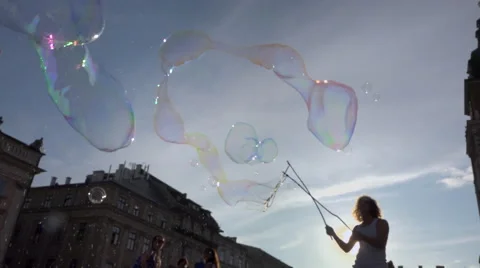 Man making very big soap bubbles on crowded square - sun back light, slow motion Stock Footage 66416038