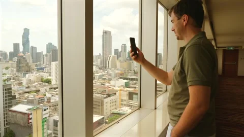 Man making video call with smartphone by window overlooking city Stock Footage 257890068