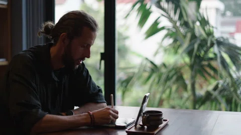 Man making video call while writing something down on his tablet Stock Footage 246406561
