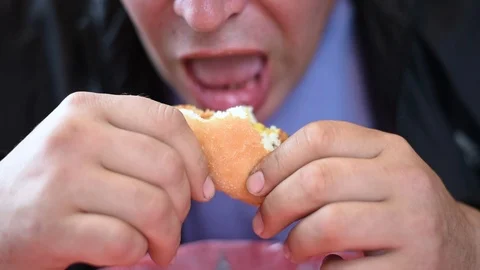 The man man eats the sandwiches hungrily biting off a big bite, drinking a drink Stock Footage 107308224