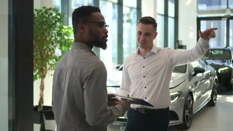 Man manager presenting new car to client and speaking, standing in dealership Stock Footage 153825788