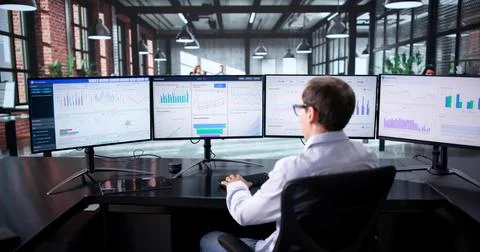Man Managing Financial Analytics Data On Multiple Computer Monitors In Office Foto stock