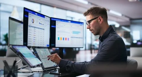 Man Managing Maintenance Requests Using Dual Touchscreen Laptops At Desk. Stock Photos