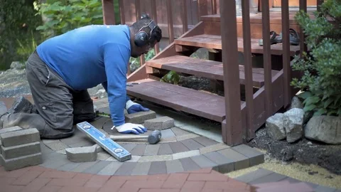 Man marking bricks for a decorative two tone paver pattern in front a stairway. Stock Footage 82096760