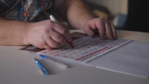 Man marks dates on calendar while sitting at table with pen and paper in home Stock Photos