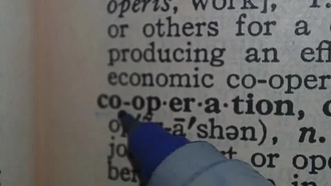 A man marks the definition from the word cooperation on a printed page with a pe Stock Footage 297276967