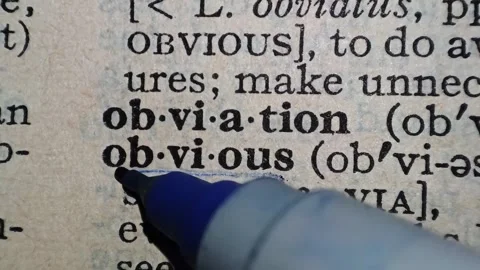 A man marks the definition from the word obvious on a printed page with a pen Stock Footage 297278243