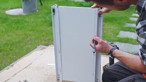 Man marks holes on drawer panel while assembling furniture on cardboard outside Stock Footage 341442728