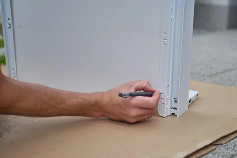 Man marks screw position with pencil on furniture panel during assembly Stock Photos