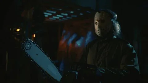 Man in the mask and with chainsaw posing in the warehouse, looking away from the Stock Photos