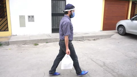 A man with a mask and face shield walking and carrying his food in plastic bags Stock Footage 140559941