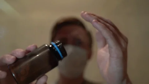 A man in a mask on a blurry background pours pills from a can on a glass table Vídeos de archivo 128840853