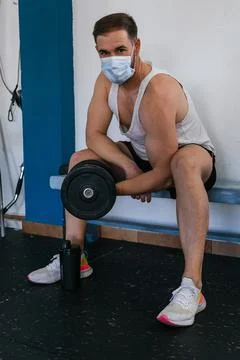 Man with mask doing biceps exercises with dumbbells in the gym. sitting on a 库存照片