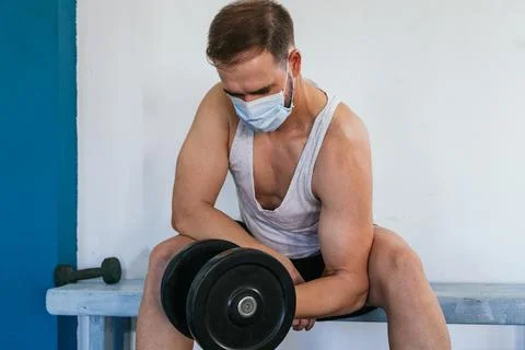 Man with mask doing biceps exercises with dumbbells in the gym. sitting on a Stock Photos