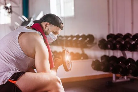 Man with mask doing biceps exercises with dumbbells in the gym. sitting on a Foto stock