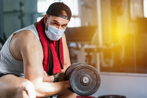 Man with mask doing biceps exercises with dumbbells in the gym. sitting on a Stock Photos