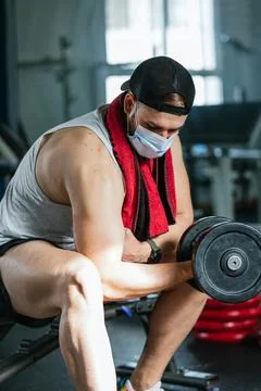 Man with mask doing biceps exercises with dumbbells in the gym. sitting on a Stock Photos