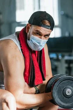 Man with mask doing biceps exercises with dumbbells in the gym. sitting on a  Stock Photos