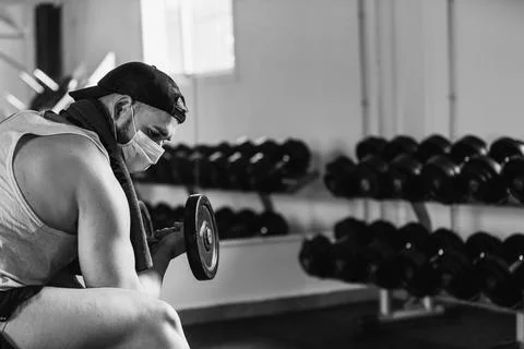 Man with mask doing biceps exercises with dumbbells in the gym. sitting on a  Stock Photos