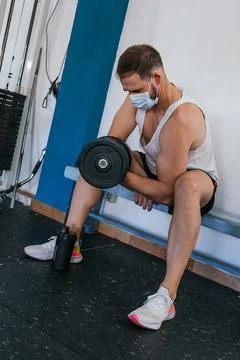 Man with mask doing biceps exercises with dumbbells in the gym. sitting on a  Stock Photos