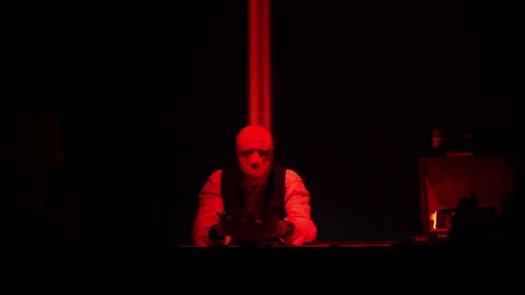 A man in a mask of an evil being sits at a table. In the hands of another mask Stock-Footage 242431788