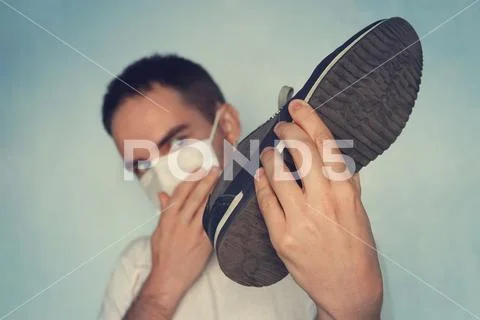 Man with mask is holding dirty stinky shoe - unpleasant smell concept. Dirty Stock Photos