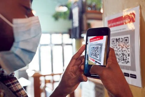 Man In Mask With Mobile Phone Checking Into Venue Scanning QR Code During Health Foto stock