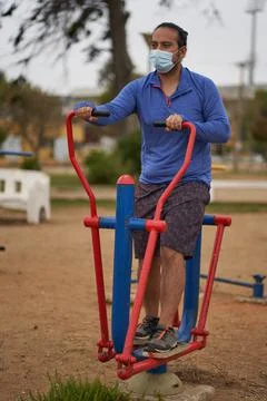 Man with mask performs elliptical exercises on machines in public square. new Stock Photos