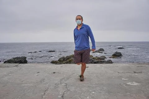 Man with mask performs relaxation exercises in front of the sea. New normalit Stock Photos