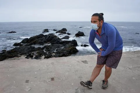 Man with mask performs stretching exercises in front of the sea. New normalit Stock Photos