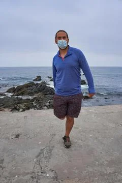 Man with mask performs yoga exercises in front of the sea. New normality. Spo Stock Photos