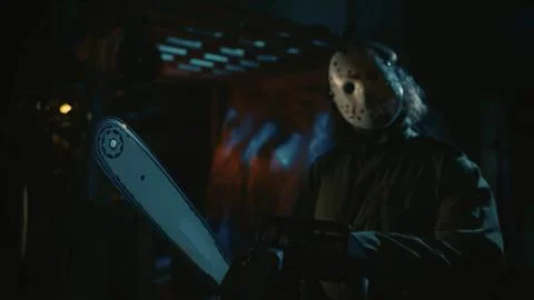 Man in the mask posing in the warehouse and holding a chainsaw, looking at the Stock Photos