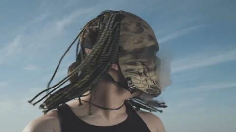 A man in the mask of a predator blows smoke from his mouth on the beach. Slow Video stock 91710403