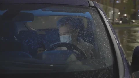 Man in mask sitting in car after work, swiping on mobile app. Freelancer looking Stock Footage 143377445