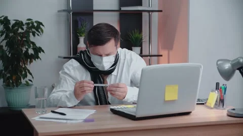 A man in a mask sitting at a table in front of a laptop looks at Video stock 147668439