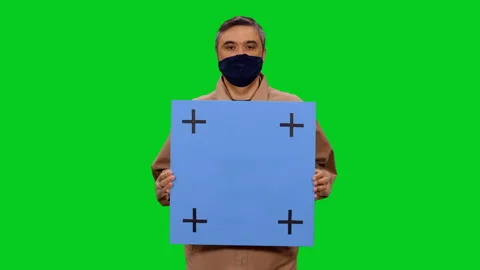 Man in mask speaking while standing with blue blank board on green screen 스톡 동영상 130796604