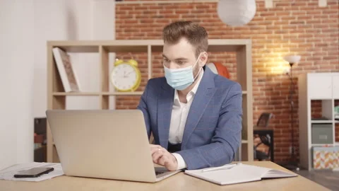 A man in a mask types something into a laptop, then writes down in a notebook 動画素材 188782794