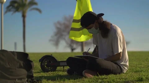 Man with mask uses tablet with digital pencil on grass next to scooter Video stock 147833731