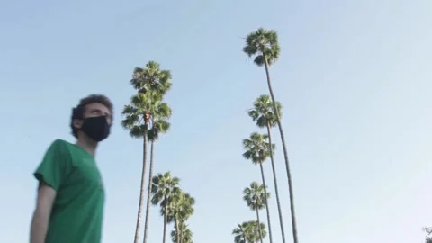 Man with Mask Walks By Palm Trees, Left to Right Stock Footage 134739215