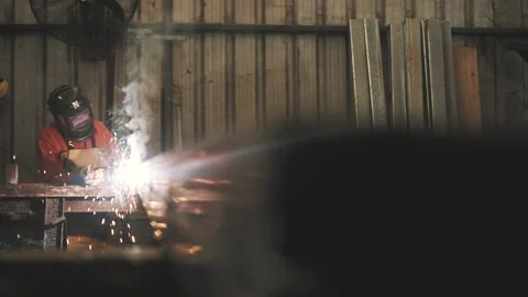 Man with a mask welds metal inside a factory and sparks fly everywhere Stock Footage 137523152
