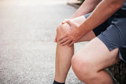 A man massaging his kneecap while suffering from patellofemoral joint pain Foto stock