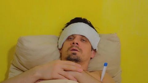 Man measures body temperature using thermometer and puts wet towel on forehead. Stock Footage 128959404