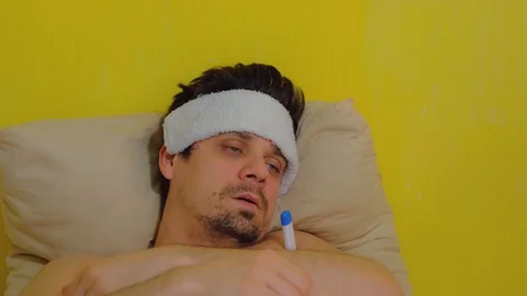 Man measures body temperature using thermometer and puts wet towel on forehead. Stock Footage 128960668