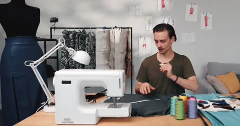 Man measures fabric for sewing clothes, sitting at working place in the atelier Stock Footage 220147124