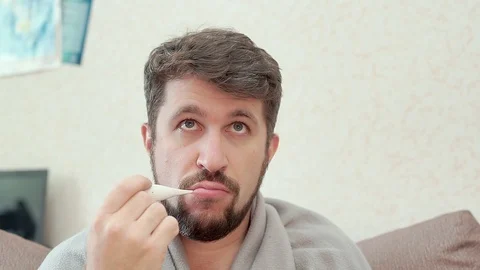 A man measures his temperature and looks at the medical thermometer 库存影片 100324880