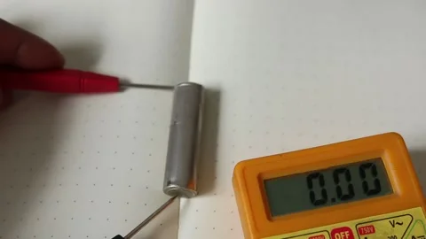 A man measures the potential (Volts) of a full capacity rechargeable AA batter u Stock Footage 239549055
